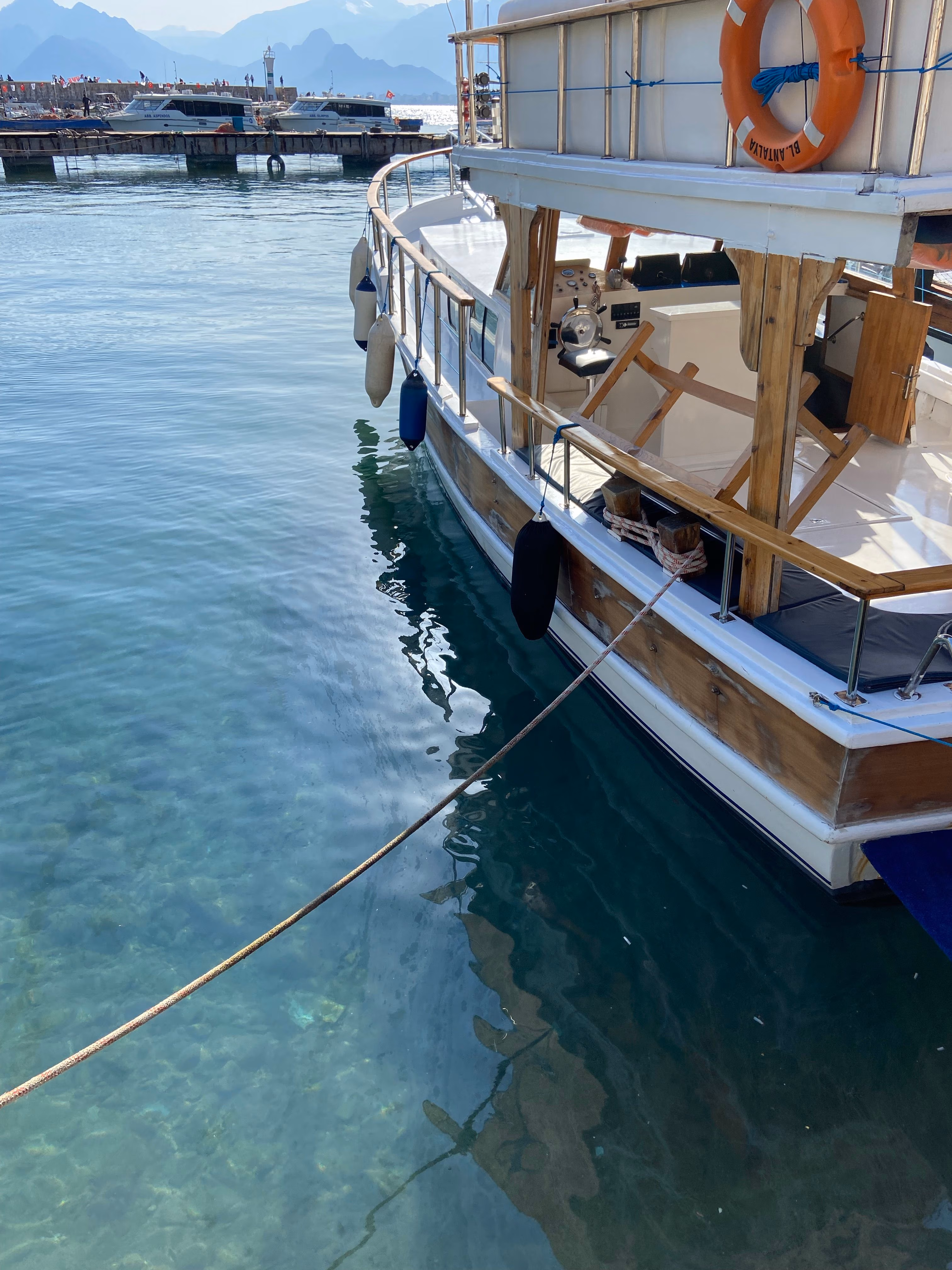Wooden boat docked in clear blue water with mountains and pier in the background.