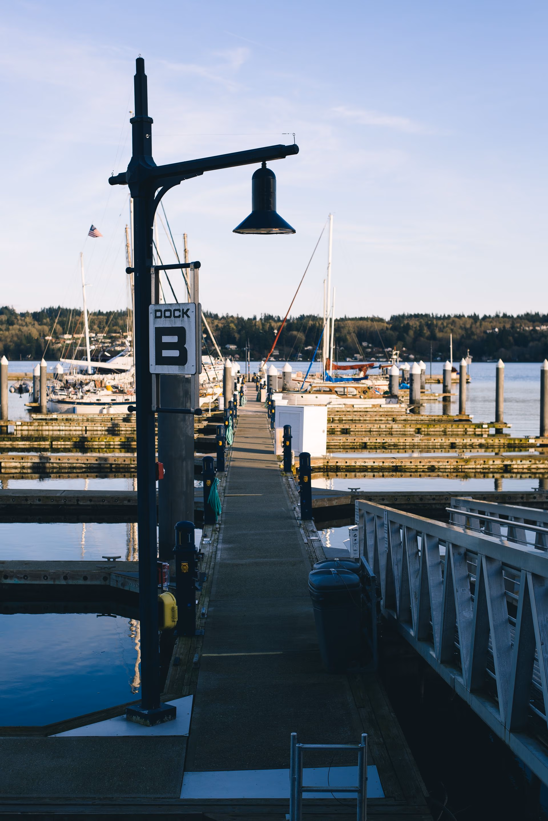 Long dock labeled B with sailboats moored on calm water under a clear blue sky.