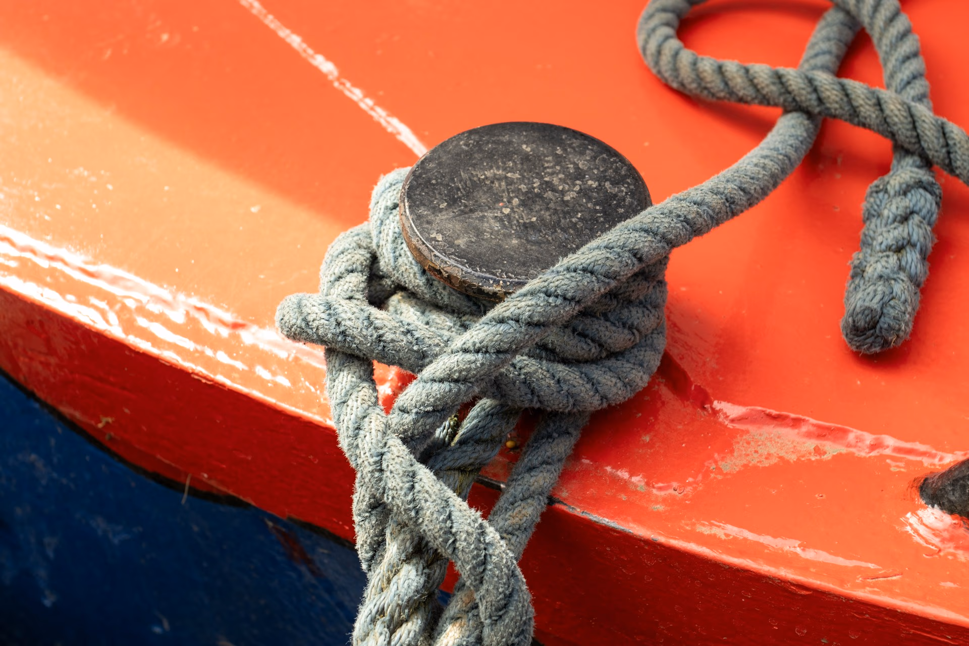 Close-up of a thick rope tied around a black cleat on a red and blue boat surface.